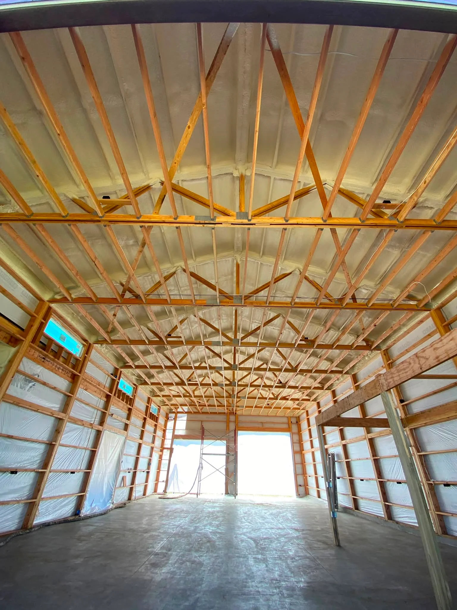 High-ceilinged post-frame building interior during construction featuring spray-foamed ceiling underside and framed timber wall structures Spray Foam Contractor